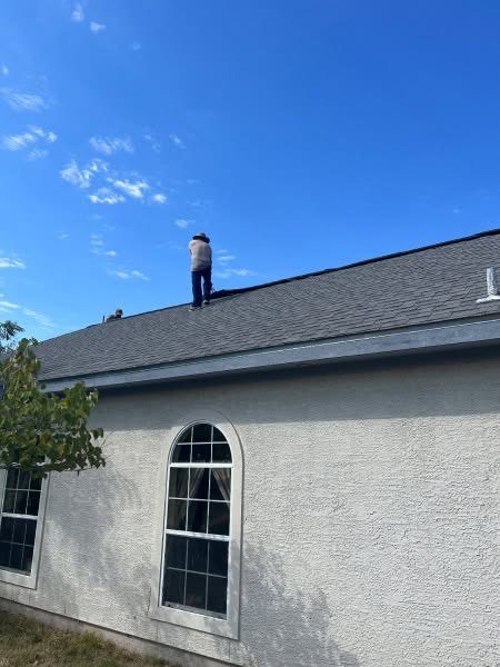 Roofer on a roof inspecting for storm damage against a clear sky